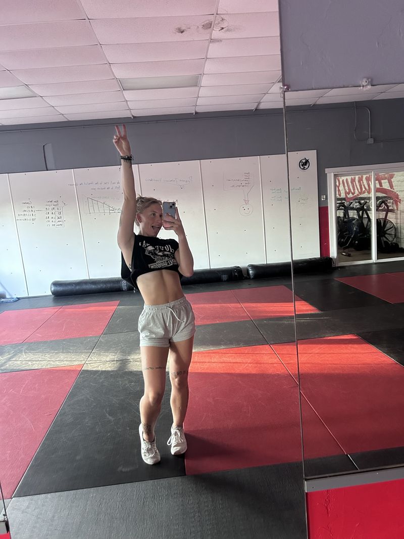 Kat throwing a peace sign in a gym mirror selfie on the mats