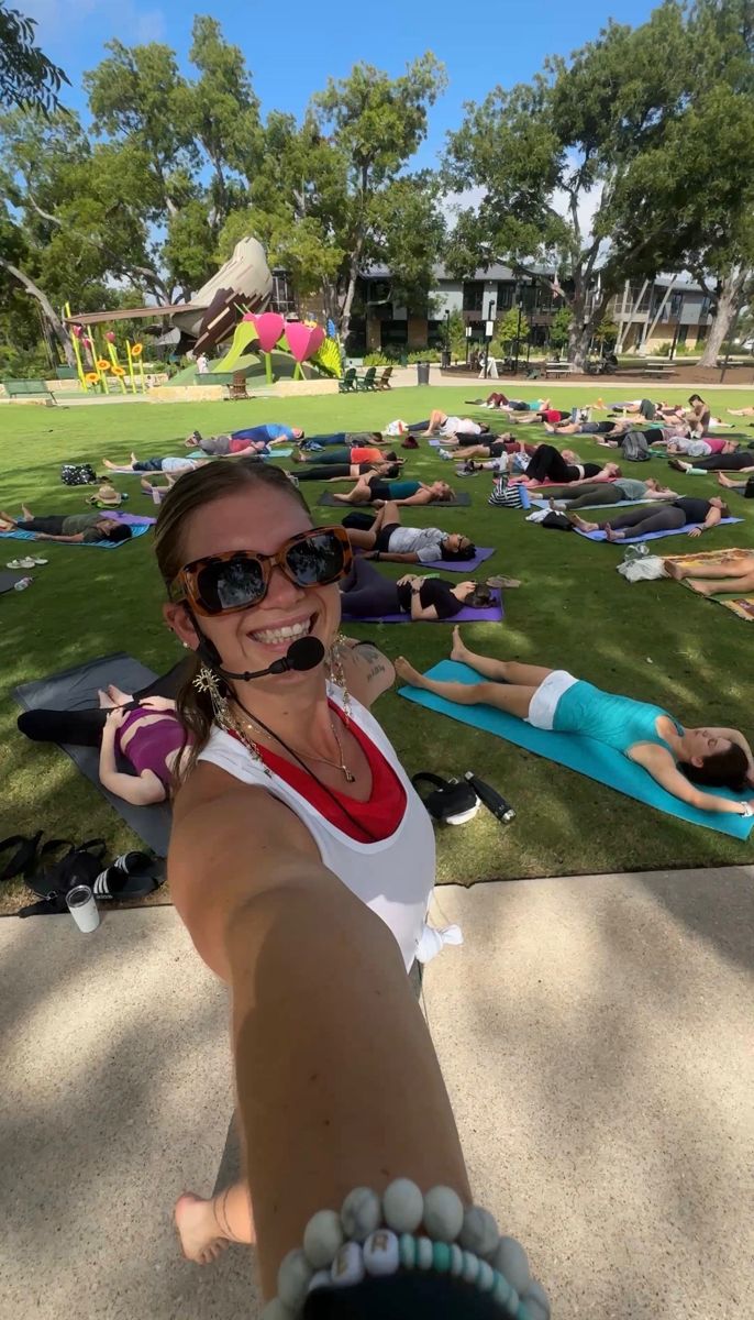 Sami taking a selfie with a headset mic while a big group rests on mats in the park